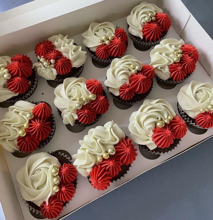 twelve cupcakes with red and white frosting in a box on a table