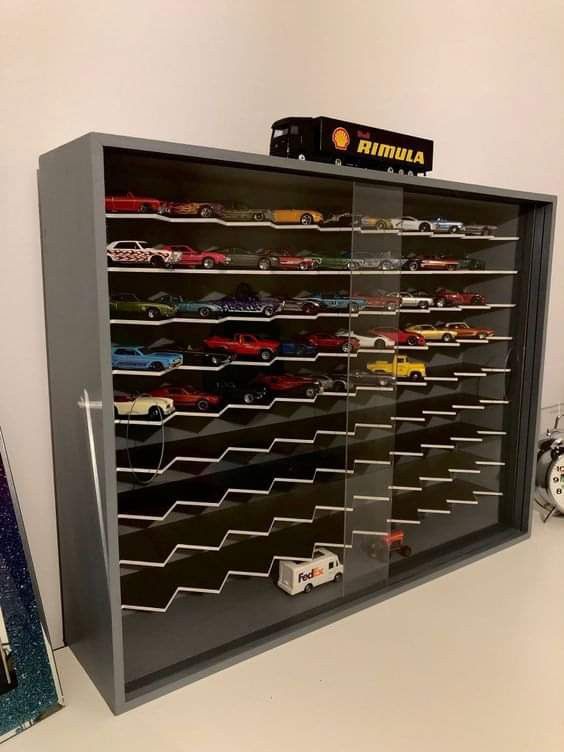 a display case filled with toy cars on top of a white table next to a clock