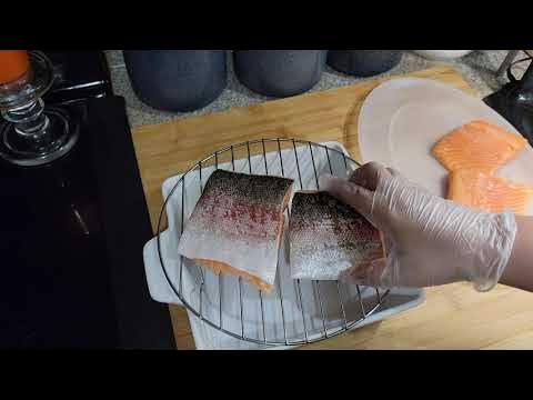 a person in white gloves is cutting fish on a grill