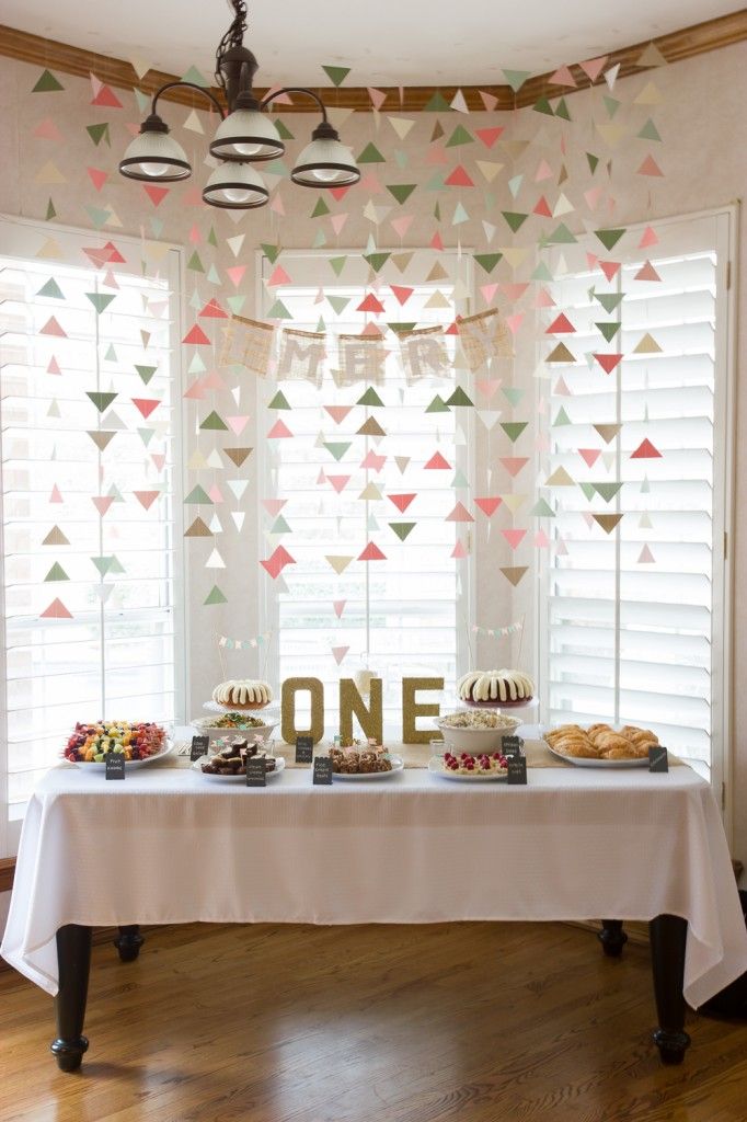 a white table topped with cakes and desserts under a window covered in paper triangles