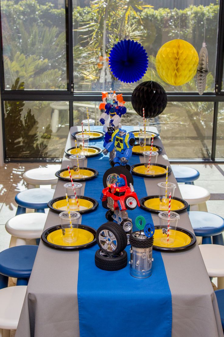 a long table set up with blue and yellow plates, black and white napkins, and balloons