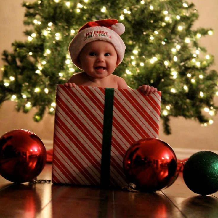 a baby wearing a santa hat sitting in a present box with christmas ornaments around it