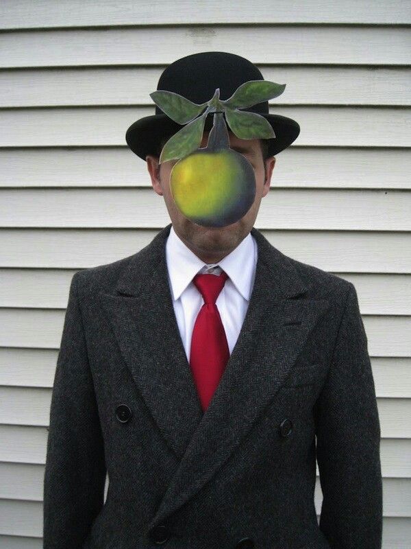 a man wearing a suit and tie with an apple painted on his face in front of him