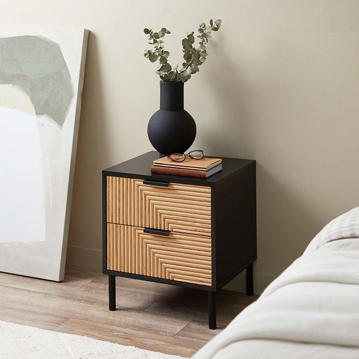 a black vase sitting on top of a wooden table next to a bed and a painting