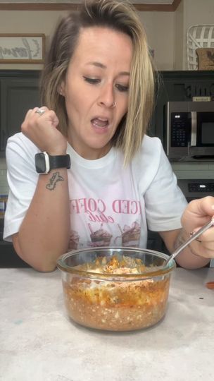 a woman sitting at a table with a bowl of food in front of her face