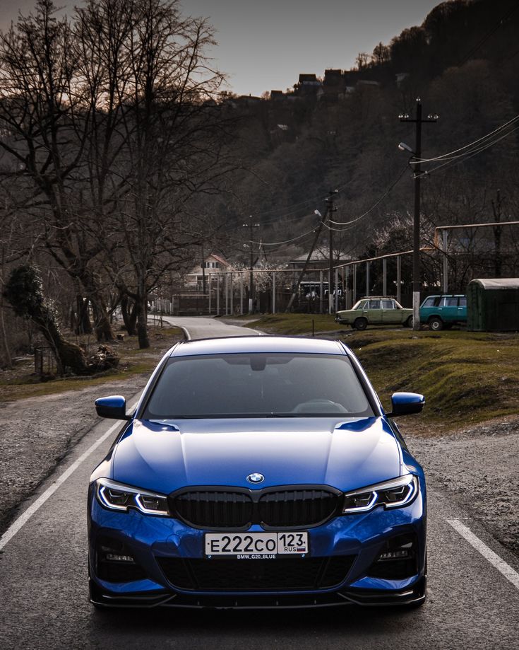 a blue car parked on the side of a road next to some trees and hills