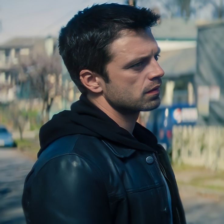 a man in a black jacket is standing on the street and looking off into the distance