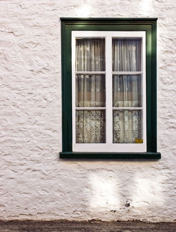 a window with curtains on the side of it in front of a white brick wall