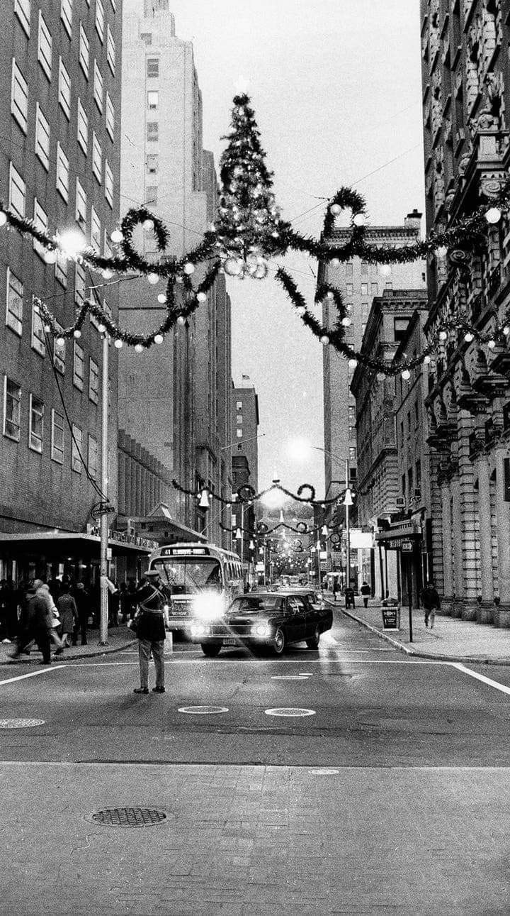 a black and white photo of cars driving down the street with christmas decorations hanging above them