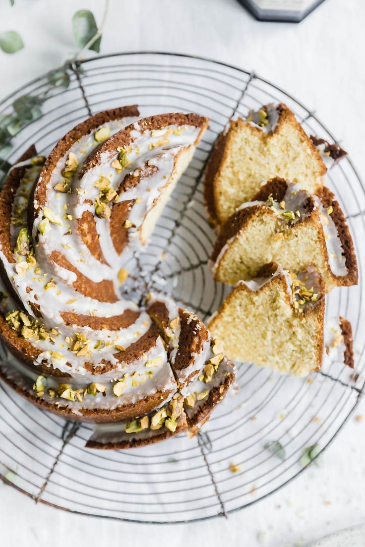 a bundt cake with white frosting and pistachio toppings on a wire rack