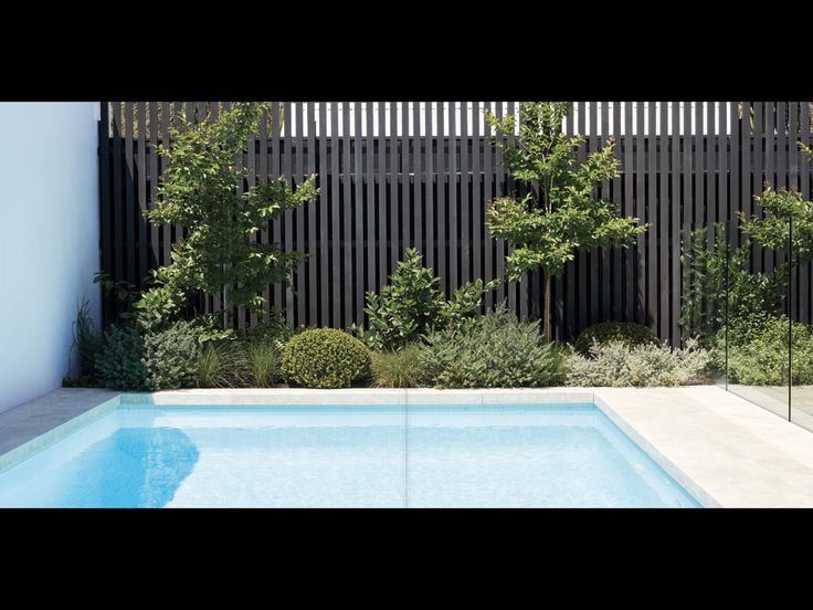 an empty swimming pool in front of a fenced in area with trees and bushes