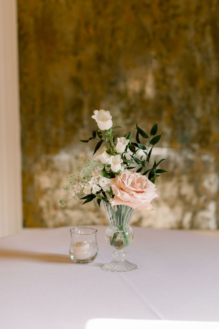 a vase filled with white and pink flowers on top of a table next to a candle