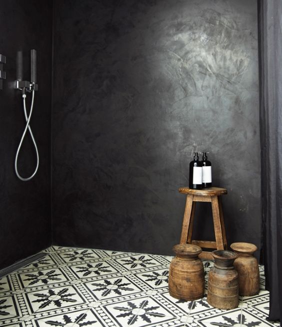 a bathroom with black walls and white tile flooring, two wooden stools in front of the shower