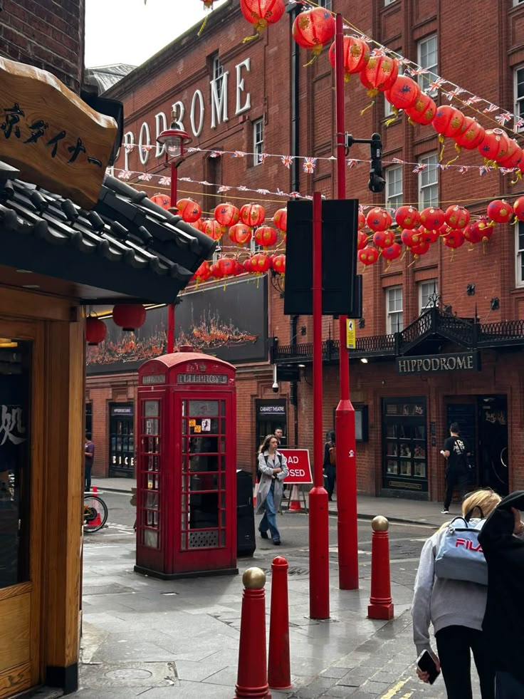 people are walking down the street in front of red telephone booths and chinese lanterns hanging above them