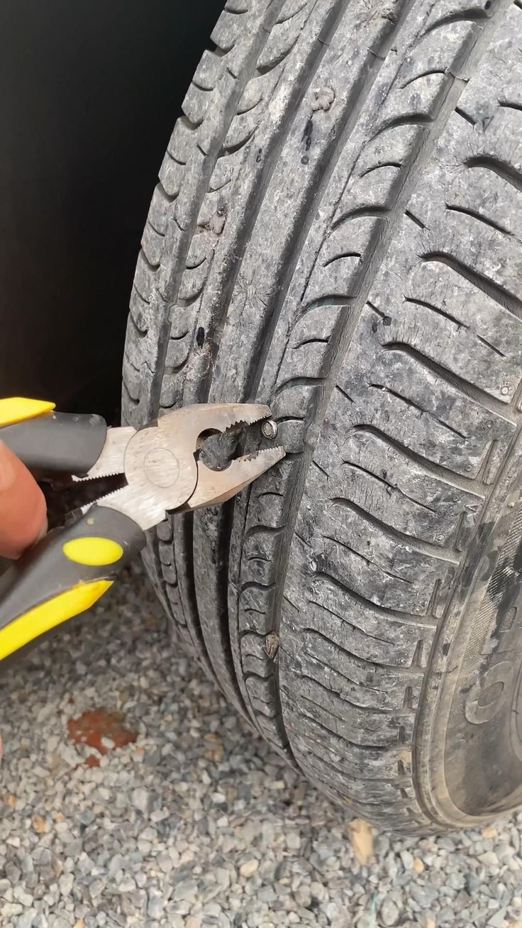 a person is holding a pair of pliers near a tire