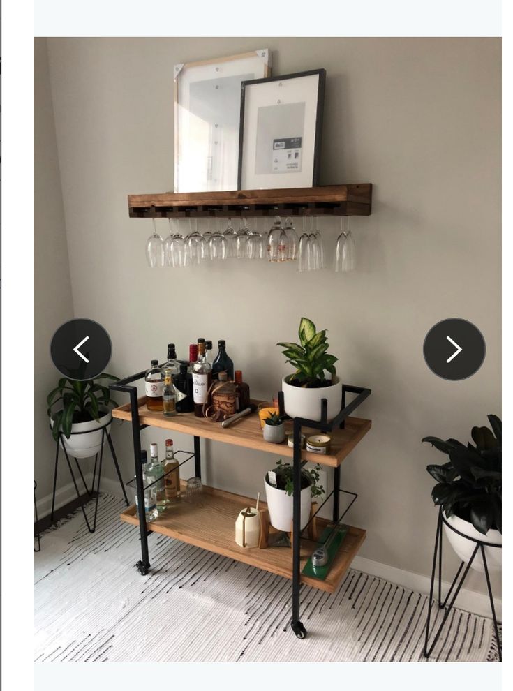 a shelf with wine glasses and bottles on it next to two potted plants in front of a mirror