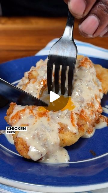 a person is holding a fork and eating some food on a blue plate with white sauce