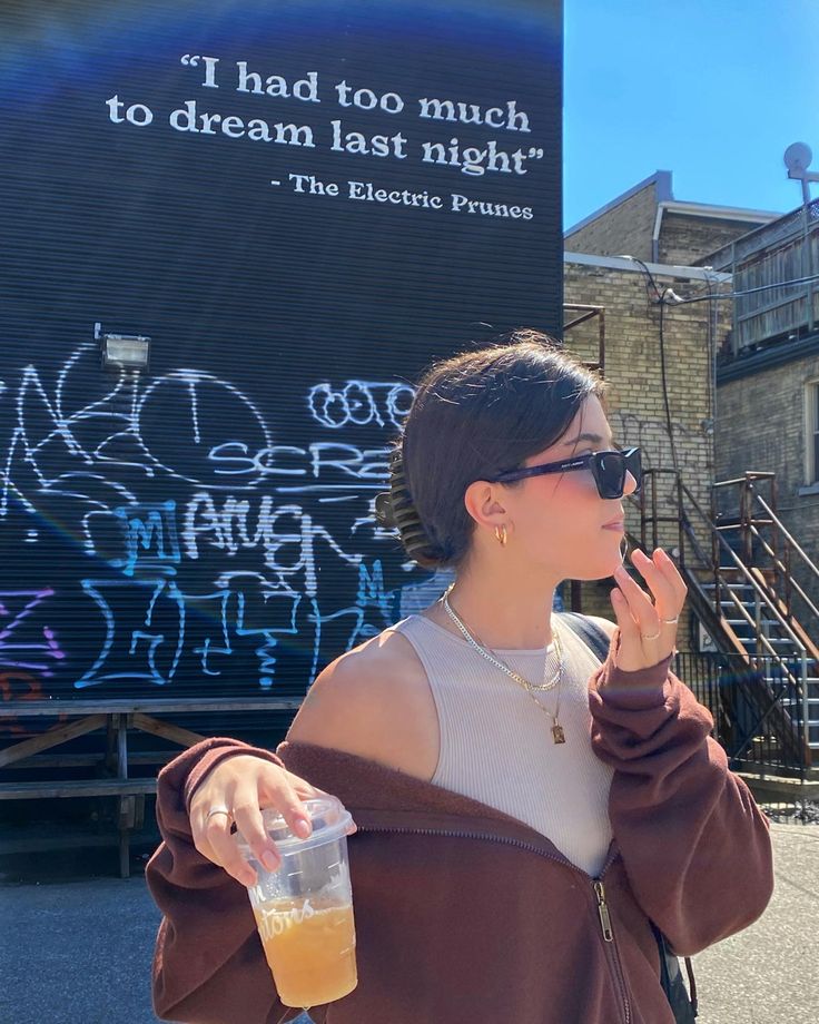 a woman standing in front of a building with graffiti on it's walls and holding a drink