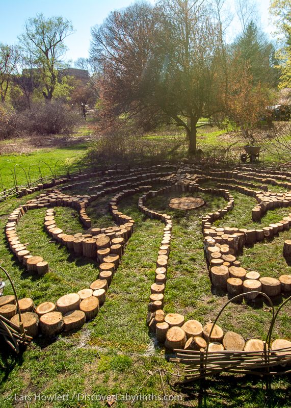 a circular garden design made out of tree trunks in the middle of a grassy area