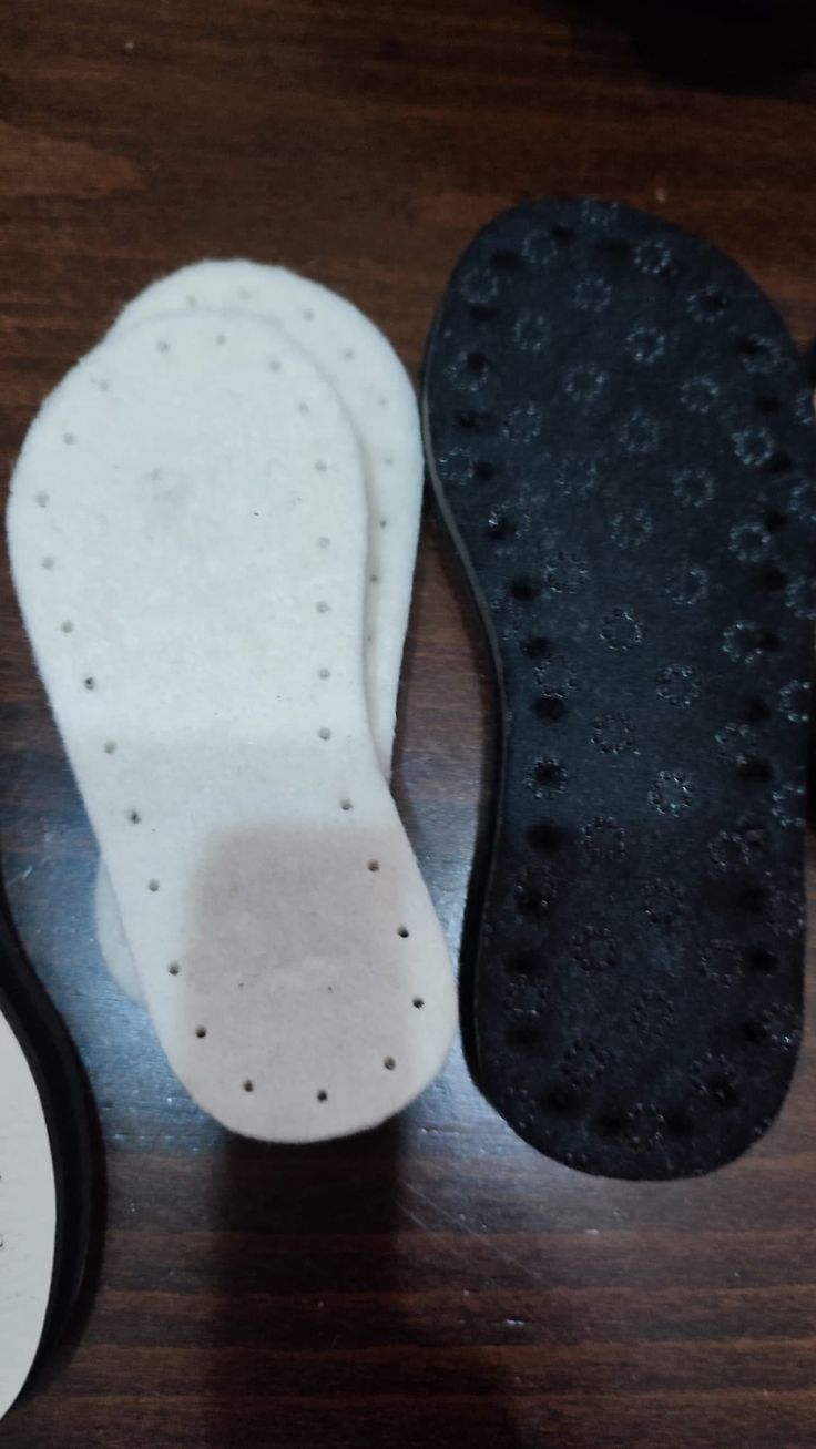 three pairs of foot pads sitting next to each other on a wooden table, one with black and white soles