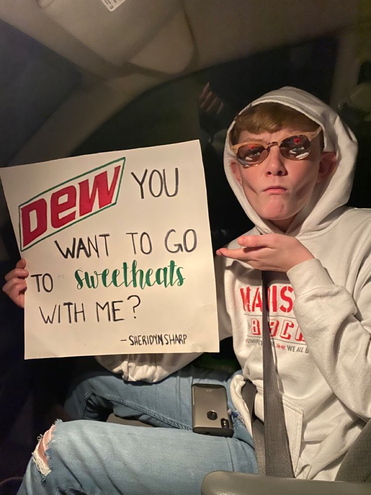 a person sitting down holding a sign that says dew you want to go to sweethearts with me?