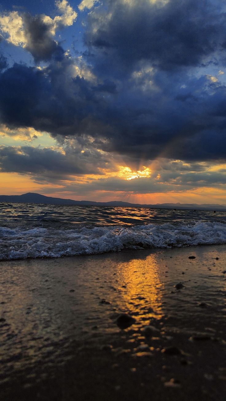 the sun is setting over the ocean with clouds in the sky and water on the beach