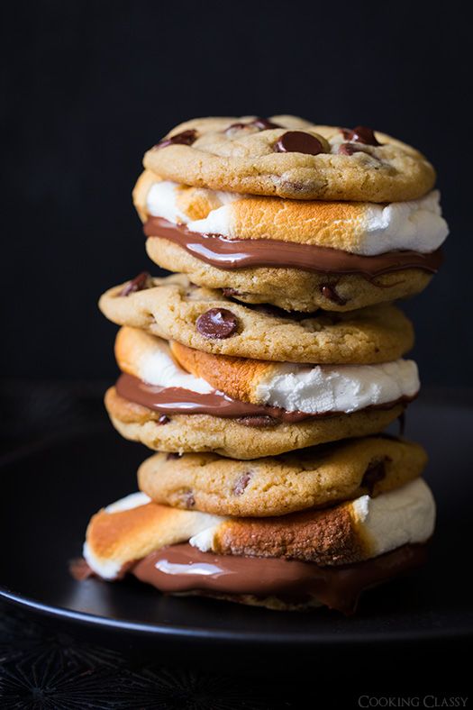 a stack of cookies with chocolate and marshmallows on top, sitting on a black plate