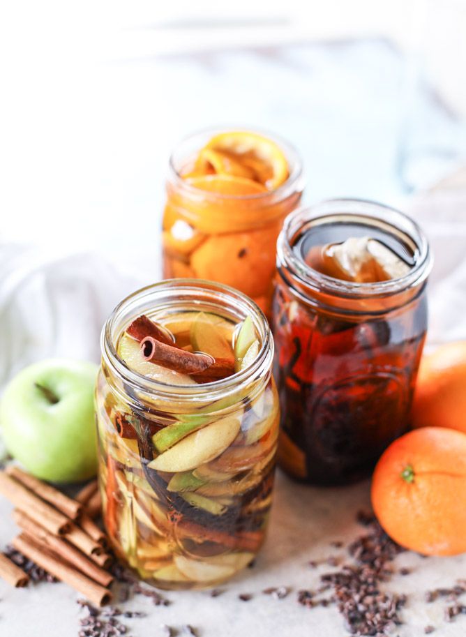 three jars filled with different types of food on top of a white table cloth next to oranges and cinnamon sticks