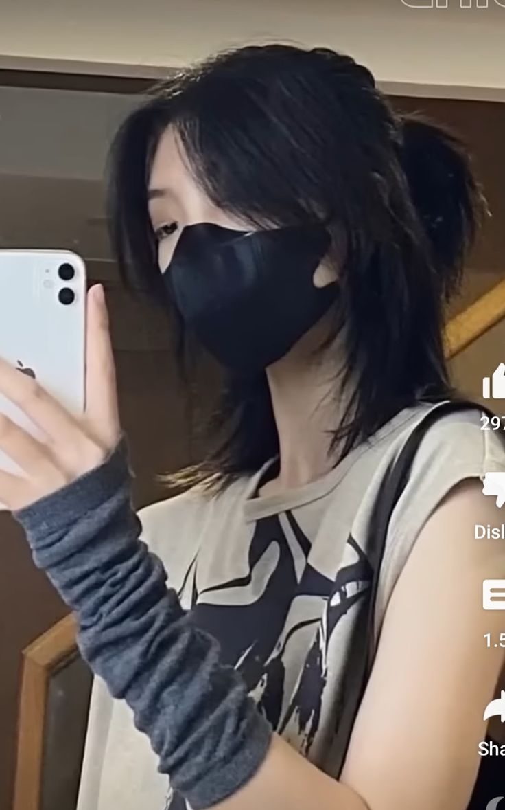 a woman wearing a black mask and holding up her cell phone