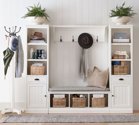 a white coat rack with baskets and hats on it next to a wall mounted shelf