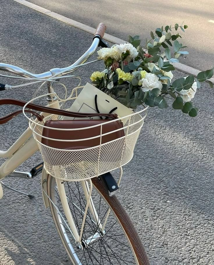 a bicycle with flowers in the basket parked on the side of the road next to an empty street