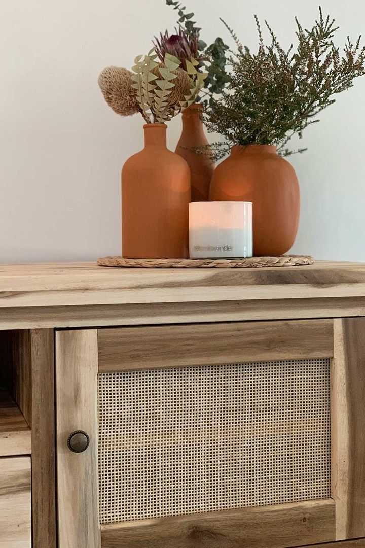 two vases sitting on top of a wooden cabinet next to a candle and some plants