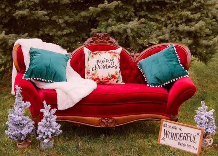 a red couch sitting on top of a lush green field next to a christmas tree