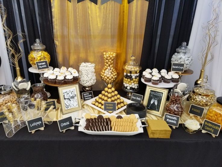 a table topped with lots of desserts and candies next to a black curtain