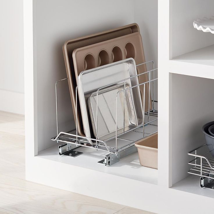 an open dish rack with plates and pans on it in a white kitchen cabinet