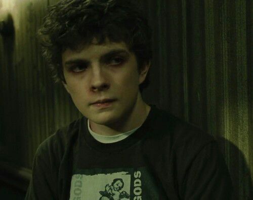 a young man in a black t - shirt is staring at the camera with an evil look on his face