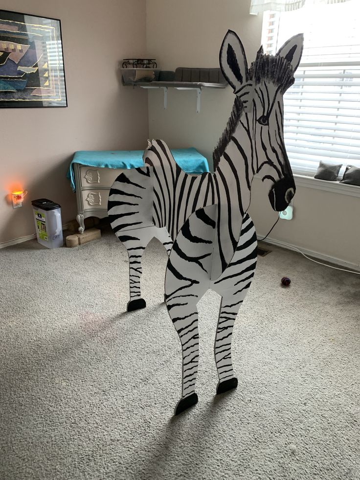 a cardboard zebra standing on top of a carpeted floor in front of a window