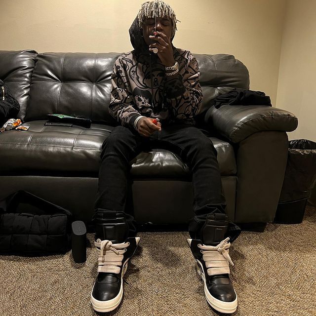 a man sitting on top of a couch in front of a black leather sofa with his feet up