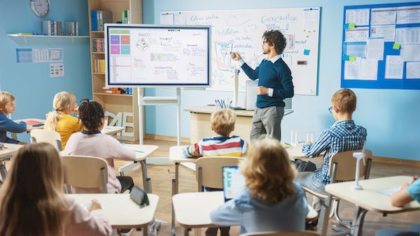 a group of children sitting at desks in front of a whiteboard