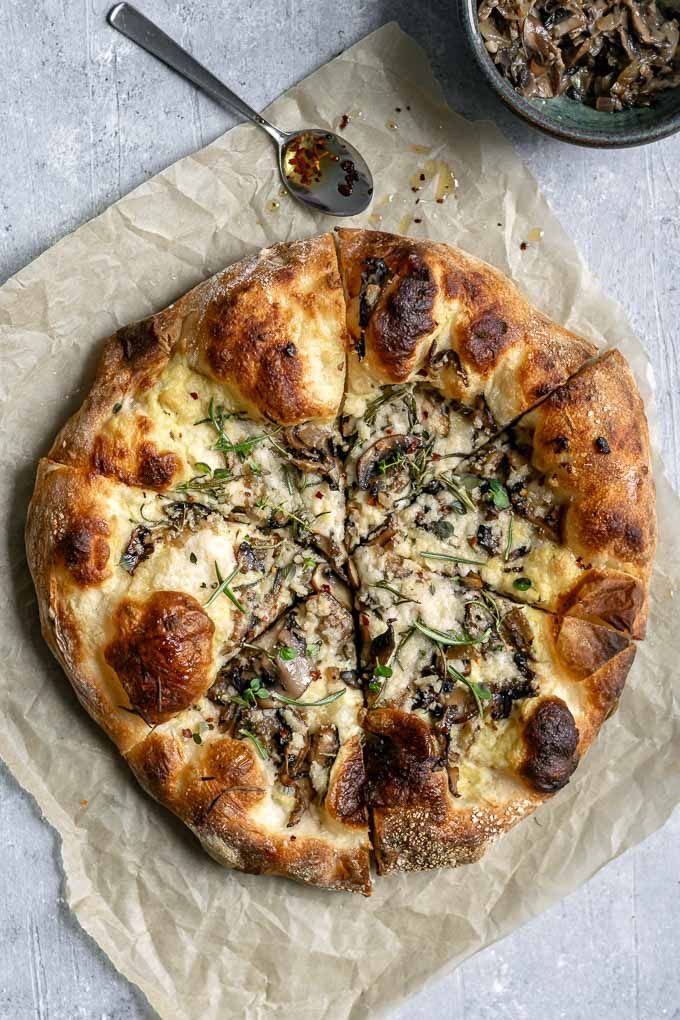 a pizza sitting on top of a piece of wax paper next to a bowl of mushrooms