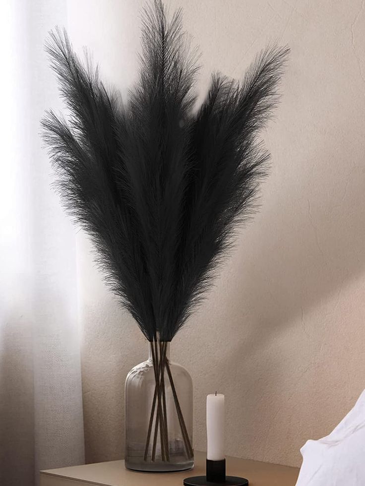 a vase with some black feathers in it on a table next to a candle and pillow