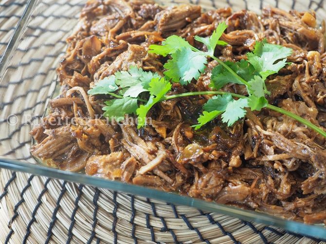 shredded meat with cilantro and parsley in a glass dish on a wicker table