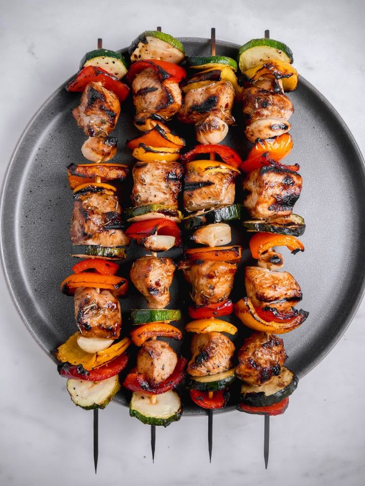 grilled chicken and vegetable kabobs on a plate with tongs in the middle