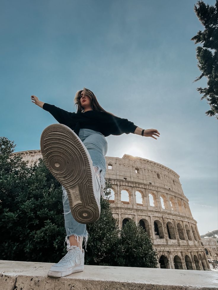 a woman standing on top of a stone wall next to the colossion in rome