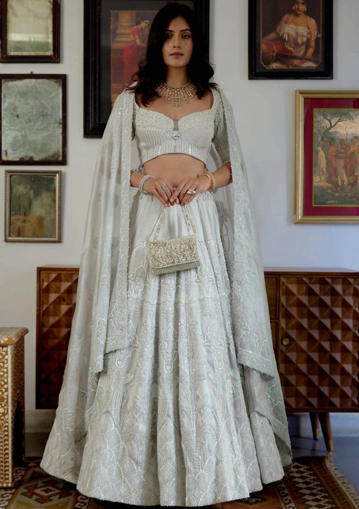 Divine is what comes to one’s mind while seeing up this moonlit beauty. Adorned with the purity of white tone and the hand-printed motifs embellished with white crystal beads and pearl moti sets up the ethereal mood for the celebrations. A perfect blend of modernity and tradition curated for the modern Indian brides. Elbow-length blouse with a sweetheart neckline adorned with white pearl moti, crystal beads, and mirror-work. Blouse contains a zip along with a metal hook on the left side. The flo Lehenga Skirt, Indian Brides, White Tone, Nehru Jackets, Western Wedding, Wedding Service, Short Suit, Mirror Work, White Crystal