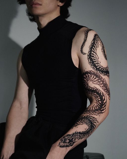 a man with a dragon tattoo on his arm is standing in front of a white wall