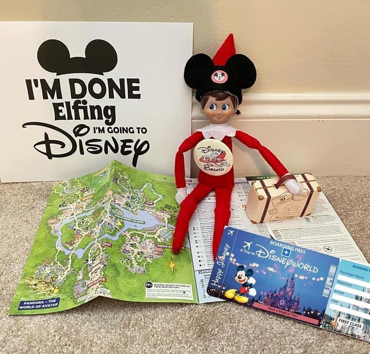 an elf is sitting on the floor next to a map and a book with mickey mouse's ears