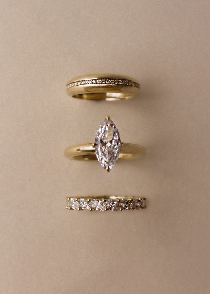 three different types of wedding rings on a beige background, one with a pear shaped diamond and the other with small round diamonds