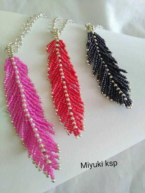 three pairs of beaded feather earrings sitting on top of a piece of white paper