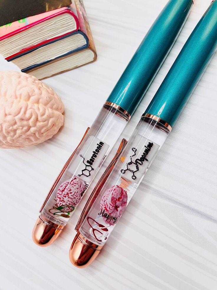 three pens sitting on top of a table next to a book and an open brain